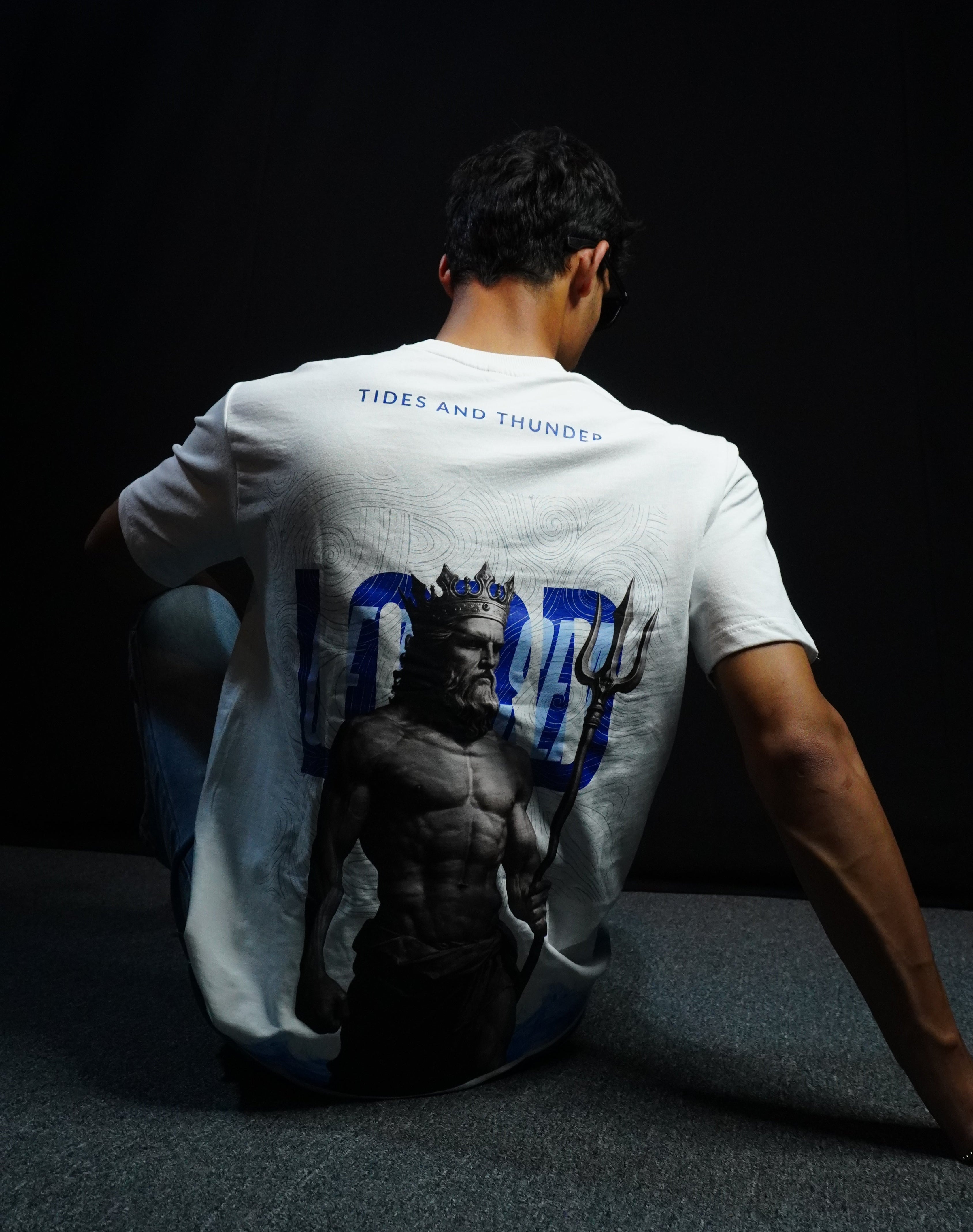 Person wearing a white t-shirt with text, standing on a dark floor.